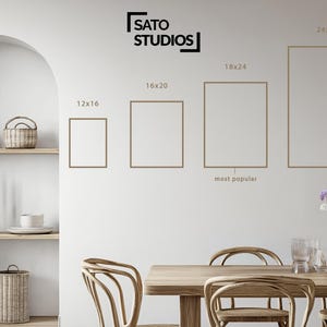K&ouml;nnte beinhalten: Ein modernes Esszimmer mit einem Holztisch und St&uuml;hlen, einer wei&szlig;en Wand mit gerahmter Kunst in verschiedenen Gr&ouml;&szlig;en und einem Regal mit dekorativen K&ouml;rben. Der Text "SATO STUDIOS" befindet sich oben.