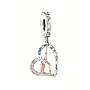 May include: Silver charm with a heart-shaped pendant. The pendant features a gymnast in a handstand pose, with the words "Never give up on your dreams" inscribed around the edge. The charm has a loop adorned with small, clear stones.