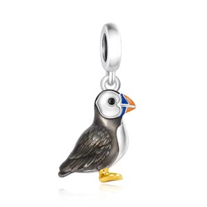 Peut inclure: Un charm en argent représentant un macareux. L'oiseau a un corps noir et blanc, un visage blanc, un bec orange et bleu et des pieds dorés. Le charm est conçu pour être ajouté à un bracelet ou un collier.