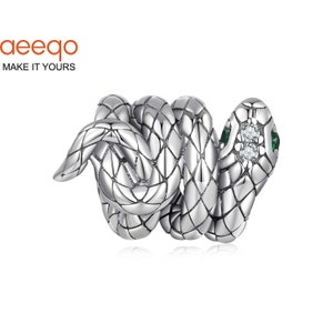 Puede incluir: Un charm de serpiente de plata con detalles en cristal verde y transparente. La serpiente está enroscada y tiene una superficie texturizada detallada.
