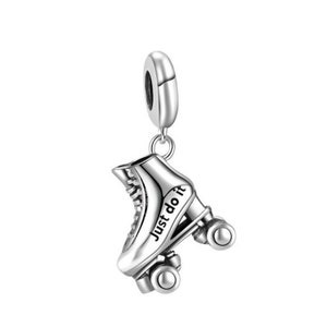 Puede incluir: Un charm de patín de ruedas plateado con el texto "Just do it" en el lateral. El charm tiene un lazo en la parte superior para sujetarlo a una pulsera o collar. El patín tiene cuatro ruedas y cordones detallados.