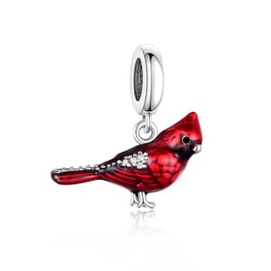 Op de afbeelding: Een rode kardinaalvogelbedel met een zilverkleurige beugel. De vogel heeft een gedetailleerd ontwerp met een glanzende afwerking en kleine, sprankelende accenten. De bedel is ontworpen om aan een armband of ketting te worden toegevoegd.