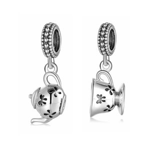 Könnte beinhalten: Silberner Charm-Set mit einer Teekanne und einer Teetasse, beide mit Blumendesigns. Die Charms haben oben eine Schlaufe zum Anbringen an einem Armband oder einer Halskette.