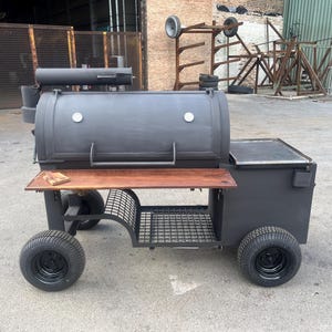 Peut inclure: Un grand barbecue fumoir noir avec une table d'appoint en bois et une étagère de rangement en métal. Le barbecue a une chambre de cuisson cylindrique et repose sur quatre pneus noirs. Un petit bloc de bois repose sur la table d'appoint.