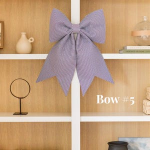 Puede incluir: Un lazo decorativo grande con un patrón de finas rayas horizontales de color morado oscuro y blanco. El lazo tiene dos bucles superiores anchos y dos colas largas y puntiagudas que cuelgan hacia abajo. El texto "Bow #5" aparece en blanco a la derecha.