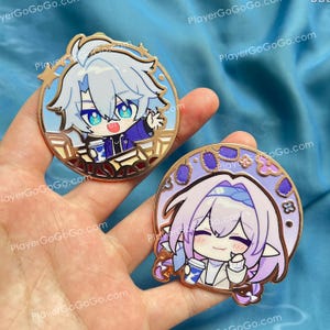 Puede incluir: Dos pines redondos de esmalte con personajes de estilo anime. Un pin tiene un fondo azul claro con un personaje sosteniendo una taza de café. El otro pin tiene un fondo morado con un personaje sosteniendo una taza de café. Ambos pines tienen bordes dorados.