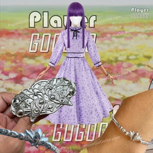 Pode incluir: Um vestido lilás com estampa floral com mangas compridas e acabamento preto, combinado com uma pulseira de prata e um grande broche de prata. O fundo apresenta o texto "Player GoGoGo".