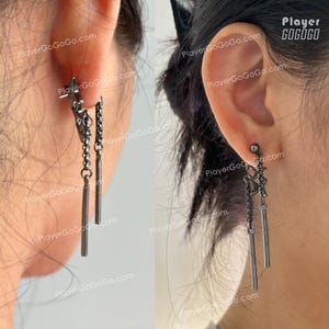 Op de afbeelding: Een paar donkergrijze oorbellen. Elke oorbel heeft een kleine stervormige stud, een ketting en twee hangende, dunne, rechthoekige staven. De oorbellen worden op het oor gedragen.