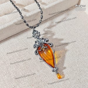 May include: A silver-toned pendant necklace featuring a large, teardrop-shaped amber stone. The amber is a warm, translucent orange color, set in an ornate, filigree-style frame. The necklace has a dark, beaded chain and a small amber drop at the bottom.