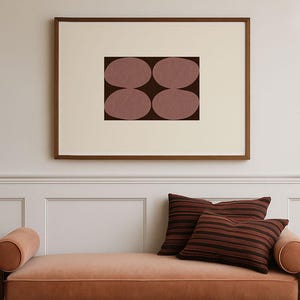 May include: A mid-century modern style chaise lounge in a warm peach color with a dark wood frame. Two striped pillows in shades of brown and red rest on the chaise. Above, a framed artwork features four oval shapes in a dark brown color.