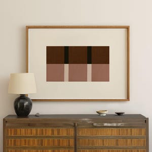 Peut inclure: Une impression d'art encadrée avec un design géométrique abstrait. L'œuvre présente des blocs rectangulaires dans des tons de marron, rose et beige, avec une bande verticale noire. L'impression est encadrée dans un cadre en bois, pour la décoration intérieure.