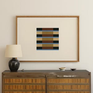 以下が含まれることがあります： 幾何学的なデザインの抽象的なアートプリント。茶色、黒、タン、青の水平な帯が対称的に配置されています。木製のフレームに収められており、インテリアに最適です。アート作品は、モダンな空間に洗練された雰囲気を加えます。