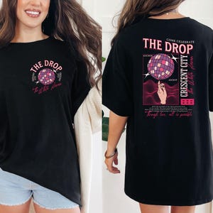 May include: Black t-shirt with a graphic design featuring a disco ball and the text "THE DROP". The design includes the words "Crescent City" and "The White Haven". The shirt has a relaxed fit.