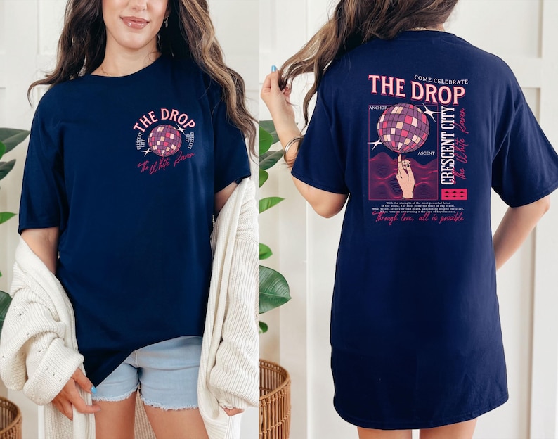May include: Navy blue t-shirt with a graphic of a disco ball and the text "The Drop". The back of the shirt features a similar design with additional text including "Crescent City" and "Anchor".