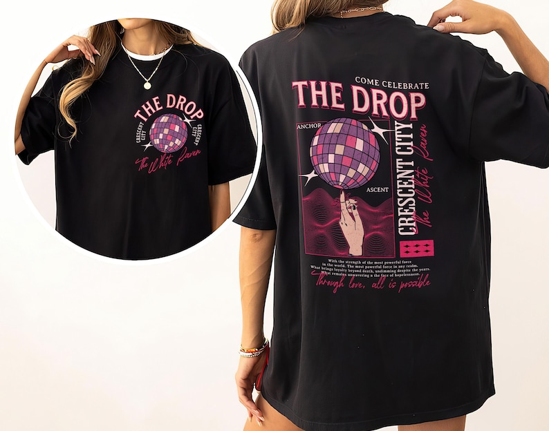 May include: Black t-shirt with a graphic design featuring the text "THE DROP" and a disco ball. The back of the shirt includes additional text: "COME CELEBRATE THE DROP CRESCENT CITY The White Paven".