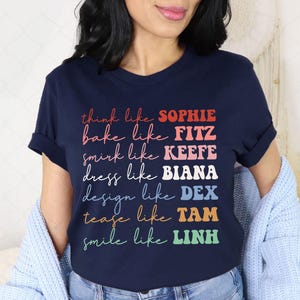 Puede incluir: Camiseta azul marino con texto colorido que dice: "think like SOPHIE, bake like FITZ, smirk like KEEFE, dress like BIANA, design like DEX, tease like TAM, smile like LINH". La camiseta es de cuello redondo.