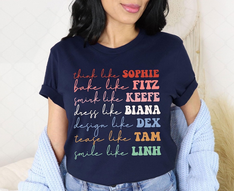 Puede incluir: Camiseta azul marino con texto colorido que dice: "think like SOPHIE, bake like FITZ, smirk like KEEFE, dress like BIANA, design like DEX, tease like TAM, smile like LINH". La camiseta es de cuello redondo.