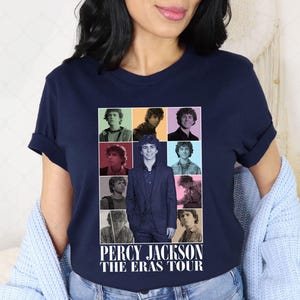 May include: Navy blue t-shirt featuring a collage of images of a person, with the text "PERCY JACKSON THE ERAS TOUR" in white. The collage has a grid layout with images in various colors. The shirt is made of a soft material.