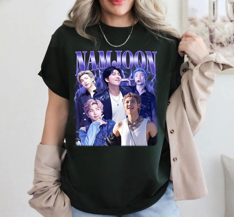 May include: Dark green t-shirt featuring a graphic of the word "NAMJOON" in purple and white, with a collage of five people. The design has a vintage, retro aesthetic with lightning bolt accents.