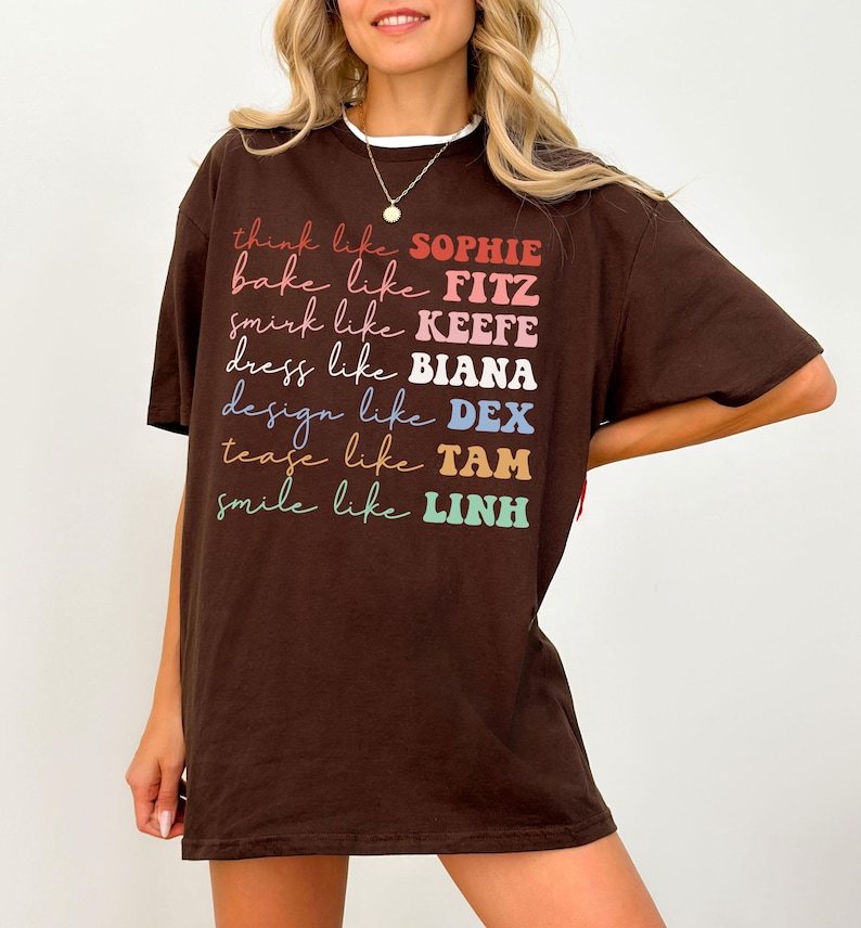 Puede incluir: Una camiseta marr&oacute;n con las frases "think like SOPHIE, bake like FITZ, smirk like KEEFE, dress like BIANA, design like DEX, tease like TAM, smile like LINH" impresas en varios colores. La camiseta tiene un cuello blanco.