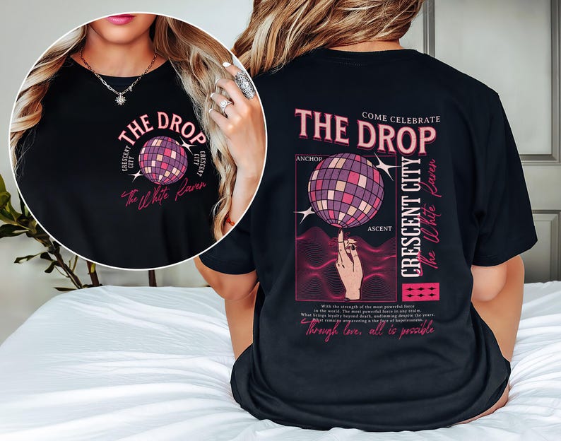 May include: Black t-shirt with a graphic design featuring a disco ball and text that reads "THE DROP" and "CRESCENT CITY". The design also includes the words "The White Raven" in a script font.