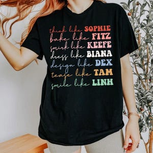 Puede incluir: Camiseta negra con texto colorido: "think like SOPHIE, bake like FITZ, smirk like KEEFE, dress like BIANA, design like DEX, tease like TAM, smile like LINH." El texto es multicolor y con diferentes fuentes.
