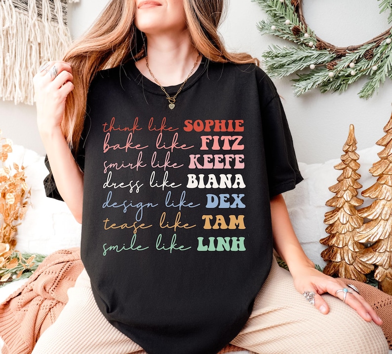 Puede incluir: Camiseta negra con texto colorido que dice "think like SOPHIE, bake like FITZ, smirk like KEEFE, dress like BIANA, design like DEX, tease like TAM, smile like LINH". La camiseta es de estilo casual.