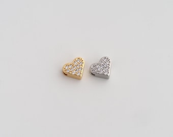 May include: Two heart-shaped charms, one gold-toned and one silver-toned, each encrusted with small, clear crystals. The charms are positioned on a white surface, showcasing their sparkling details and romantic design. Ideal for jewelry making or crafting.