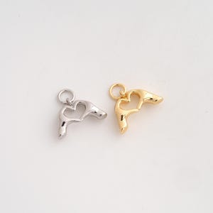 Può includere: Due ciondoli in metallo a forma di mani che formano un cuore. Un ciondolo ha una finitura color argento lucido, mentre l'altro ha una finitura color oro lucido. Ogni ciondolo presenta un piccolo anellino circolare fissato sulla parte superiore.