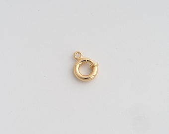 Pode incluir: Um fecho de anel de mola dourado, um componente de joalharia, é mostrado sobre um fundo branco. O fecho é circular com um pequeno laço e um mecanismo de mola para um fecho seguro. O metal tem um acabamento polido.