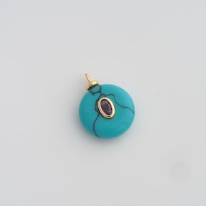 May include: A circular turquoise pendant with a gold bail. It features a small, oval amethyst stone set in a gold bezel. The turquoise has dark veining.