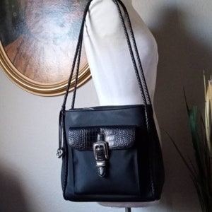 Może przedstawiać: Czarna torebka na ramię z kieszenią z krokodylej sk&oacute;ry i srebrną klamrą. Torebka ma pleciony pasek.