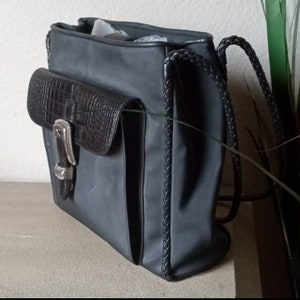 Może przedstawiać: Czarna sk&oacute;rzana torba typu tote z plecionym paskiem i mniejszą kieszenią z krokodylą fakturą z przodu. Torba ma srebrną klamrę i zamek błyskawiczny.