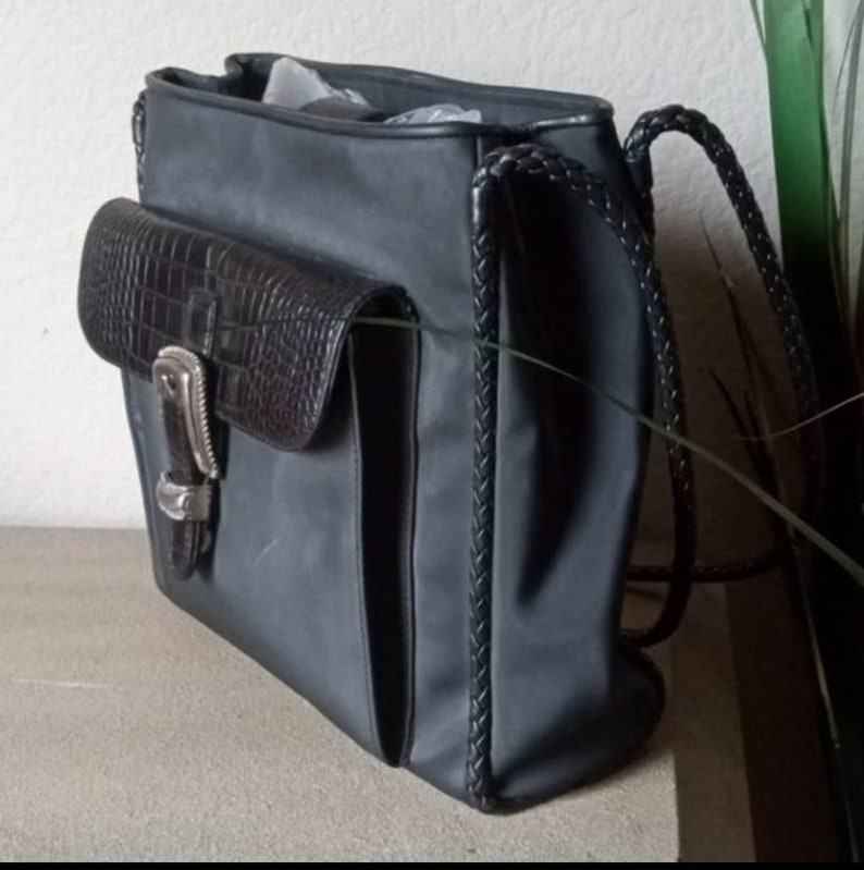 Może przedstawiać: Czarna sk&oacute;rzana torba typu tote z plecionym paskiem i mniejszą kieszenią z krokodylą fakturą z przodu. Torba ma srebrną klamrę i zamek błyskawiczny.