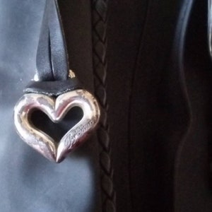 Może przedstawiać: Czarna sk&oacute;rzana torebka z srebrnym, sercowatym brelokiem z napisem "Braccialini".