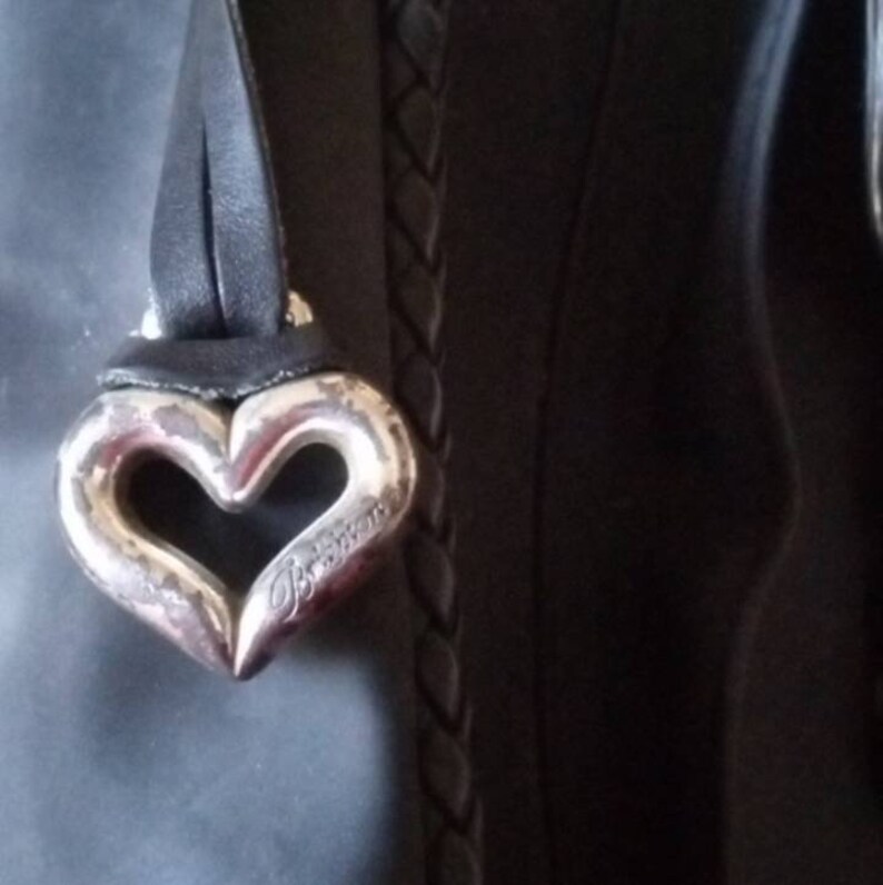 Może przedstawiać: Czarna sk&oacute;rzana torebka z srebrnym, sercowatym brelokiem z napisem "Braccialini".