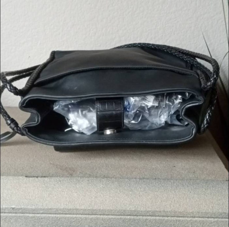 Może przedstawiać: Czarna sk&oacute;rzana torebka z plecionym paskiem i srebrną klamrą. Torebka jest otwarta i pusta.