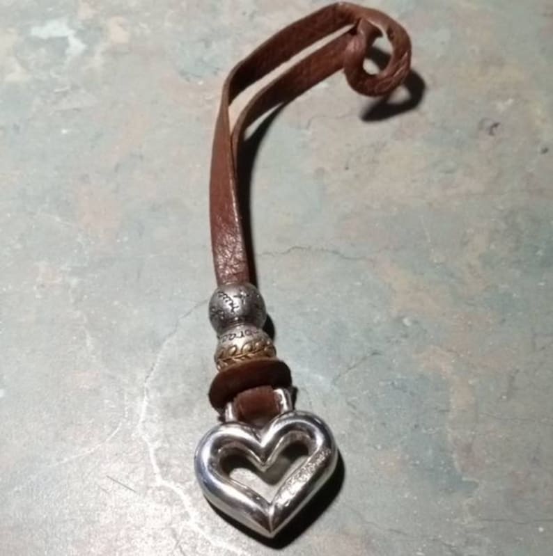 May include: A brown leather cord necklace with silver and gold beads and a silver heart charm.