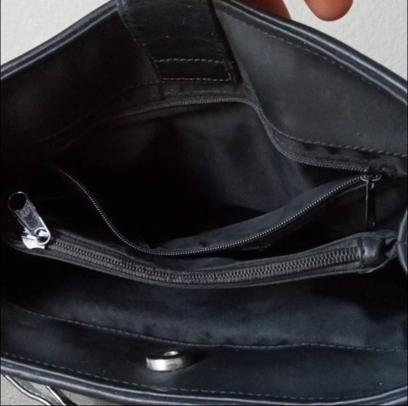 Może przedstawiać: Czarna sk&oacute;rzana torebka z kieszenią zapinaną na zamek błyskawiczny i zatrzaskiem. Torebka jest otwarta i widać wnętrze.