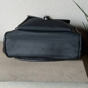 Może przedstawiać: Czarna torebka z nylonu z plecionym wykończeniem i srebrną klamrą.