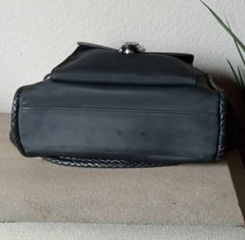 Może przedstawiać: Czarna torebka z nylonu z plecionym wykończeniem i srebrną klamrą.