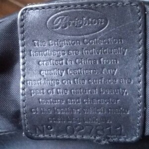 Może przedstawiać: Zbliżenie na czarną sk&oacute;rzaną metkę z logo Brighton i tekstem "The Brighton Collection handbags are individually crafted in China from quality leathers. Any markings on the surface are part of the natural beauty, texture and character of the leather which makes each bag unique." Metka zawiera r&oacute;wnież numer "N&deg; 027811" nadrukowany na niej.
