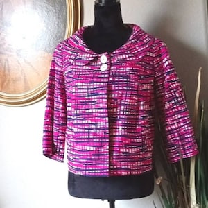 May include: A pink and white striped jacket with a white collar and two white buttons. The jacket has a slightly cropped length and three-quarter sleeves.