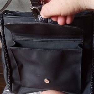 Może przedstawiać: Czarna torba typu tote z nylonu z plecionym paskiem i kieszenią zapinaną na zamek błyskawiczny. Torba ma mniejszą kieszeń z przodu i zapięcie na zatrzask.