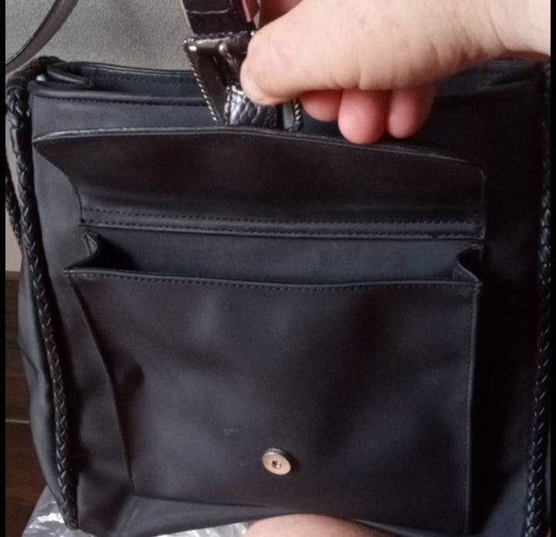 Może przedstawiać: Czarna torba typu tote z nylonu z plecionym paskiem i kieszenią zapinaną na zamek błyskawiczny. Torba ma mniejszą kieszeń z przodu i zapięcie na zatrzask.