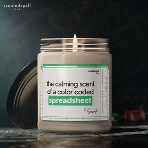 May include: A lit scented candle in a glass jar with a black lid. The label reads "the calming scent of a color coded spreadsheet" with the name "Sarah" below. The candle is labeled "Coconut Cream + Cardamom".