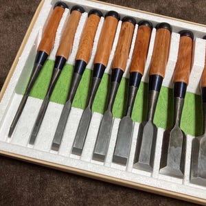 May include: A set of ten wood chisels with wooden handles and metal blades, arranged in a box with green padding. The chisels have a variety of blade shapes, suitable for woodworking and carving.
