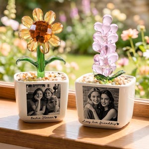 Pode incluir: Duas esculturas decorativas de flores em vasos brancos com fotos a preto e branco. Uma tem uma flor de cristal amarela e laranja, a outra uma flor de cristal rosa. Os vasos têm as frases "Bestie Forever" e "Long live friendship".