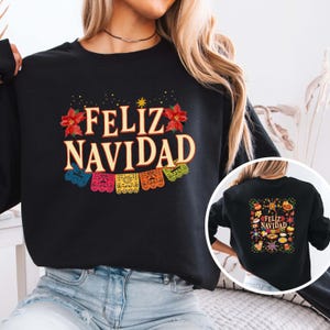 May include: Black sweatshirt with the words "FELIZ NAVIDAD" in a festive font, adorned with red poinsettias and colorful papel picado banners. A smaller image on the back repeats the design. A perfect holiday gift.