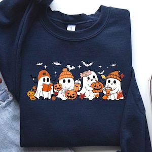 May include: A navy blue crewneck sweatshirt featuring a graphic print of four white ghosts wearing orange beanies. The ghosts are surrounded by orange pumpkins, autumn leaves, bats, and stars. One ghost holds a book, another a drink, and one a pumpkin.